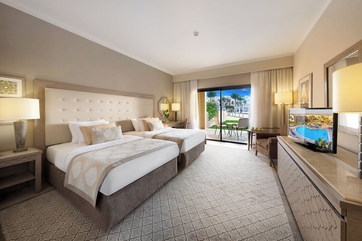 A hotel room with two beds, a television, and a balcony with a pool view.