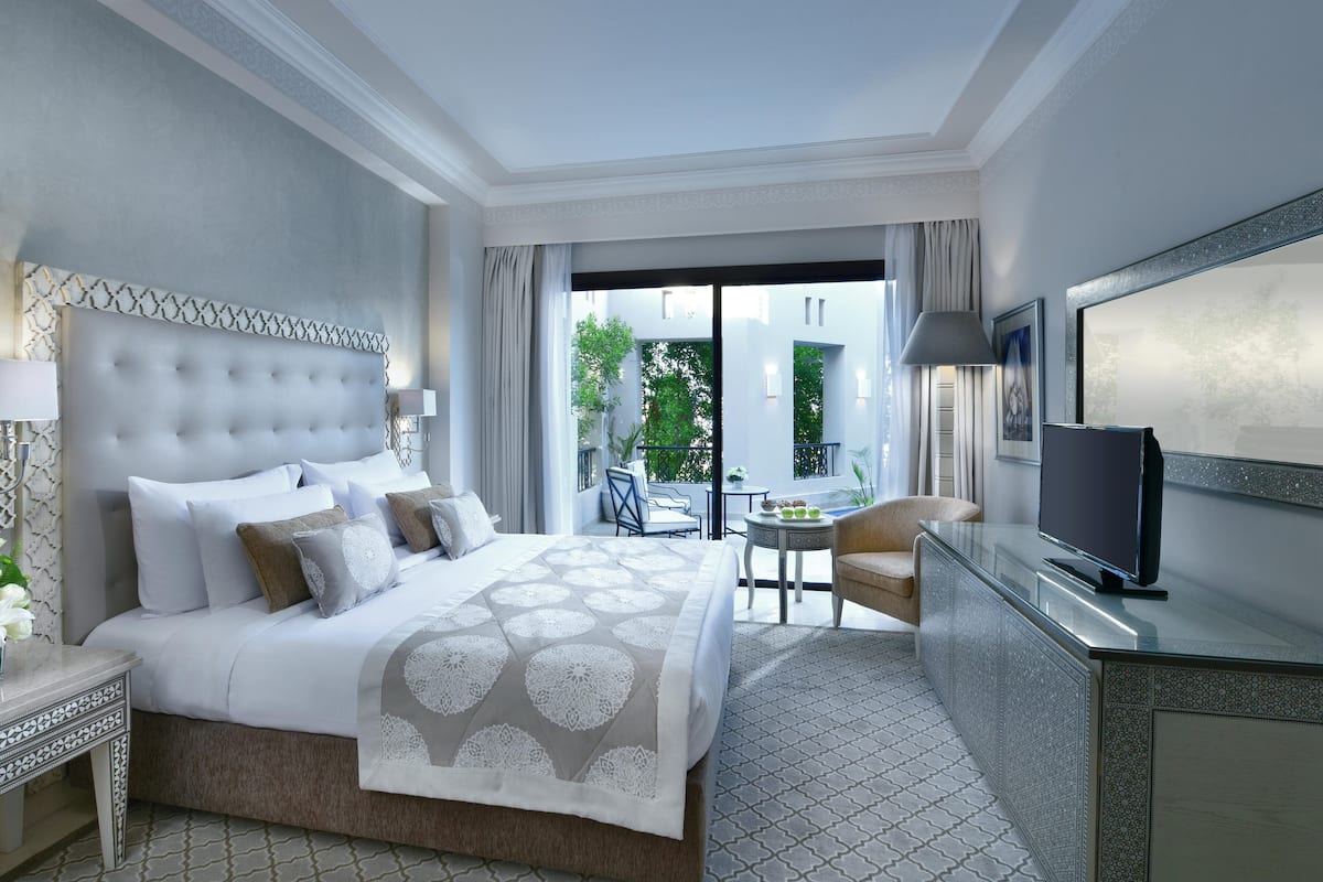 A hotel room with a large bed, a TV, a desk, and a balcony with a table and chairs.