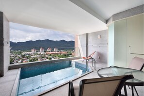 Un balcón con piscina, una mesa de vidrio y sillas, con vistas a un paisaje urbano y montañas.