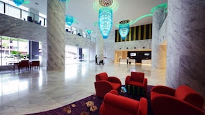 Un hall d’entrée spacieux, orné de colonnes en marbre, de sièges rouges et de lustres modernes.