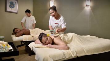 A massage therapy room with two clients receiving treatment, a therapist attending to one client, and another person standing by.