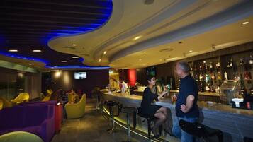 A bar area with high stools, a bar counter, and a television screen.