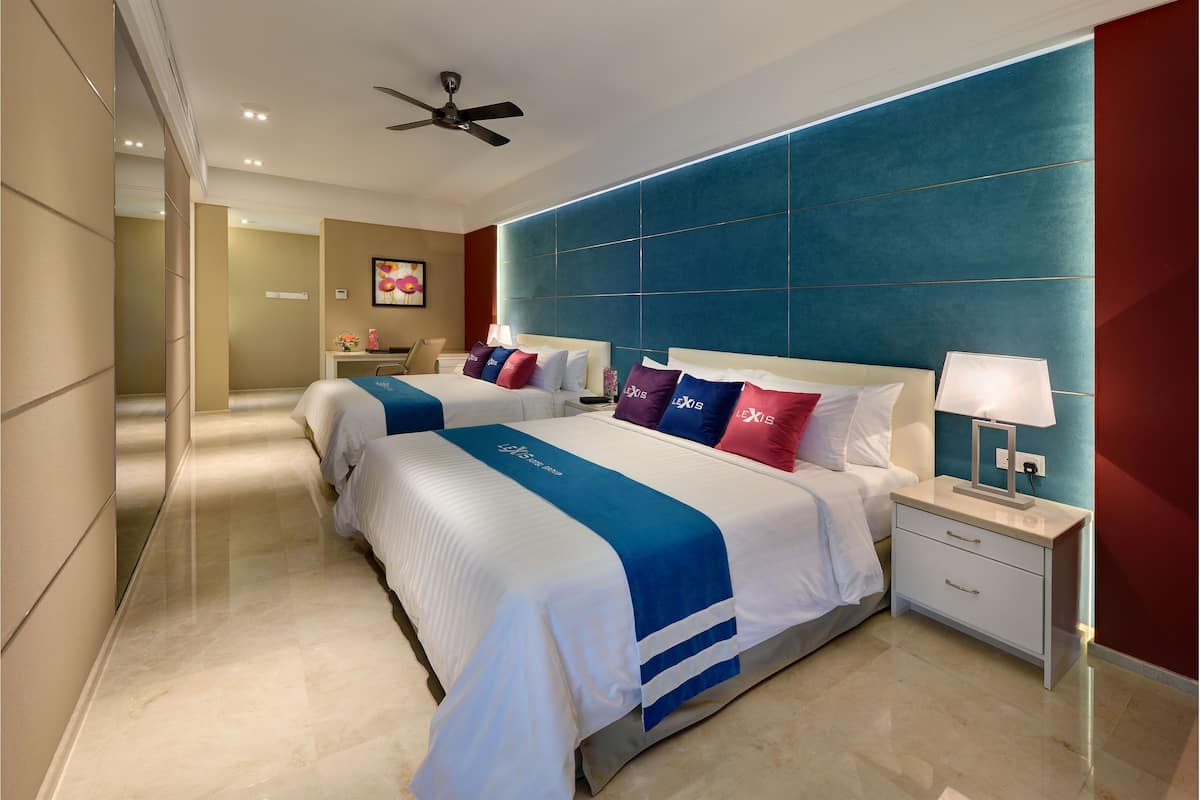 Una habitación de hotel con dos camas, una mesita de noche con lámpara, ventilador de techo y un ventanal grande.