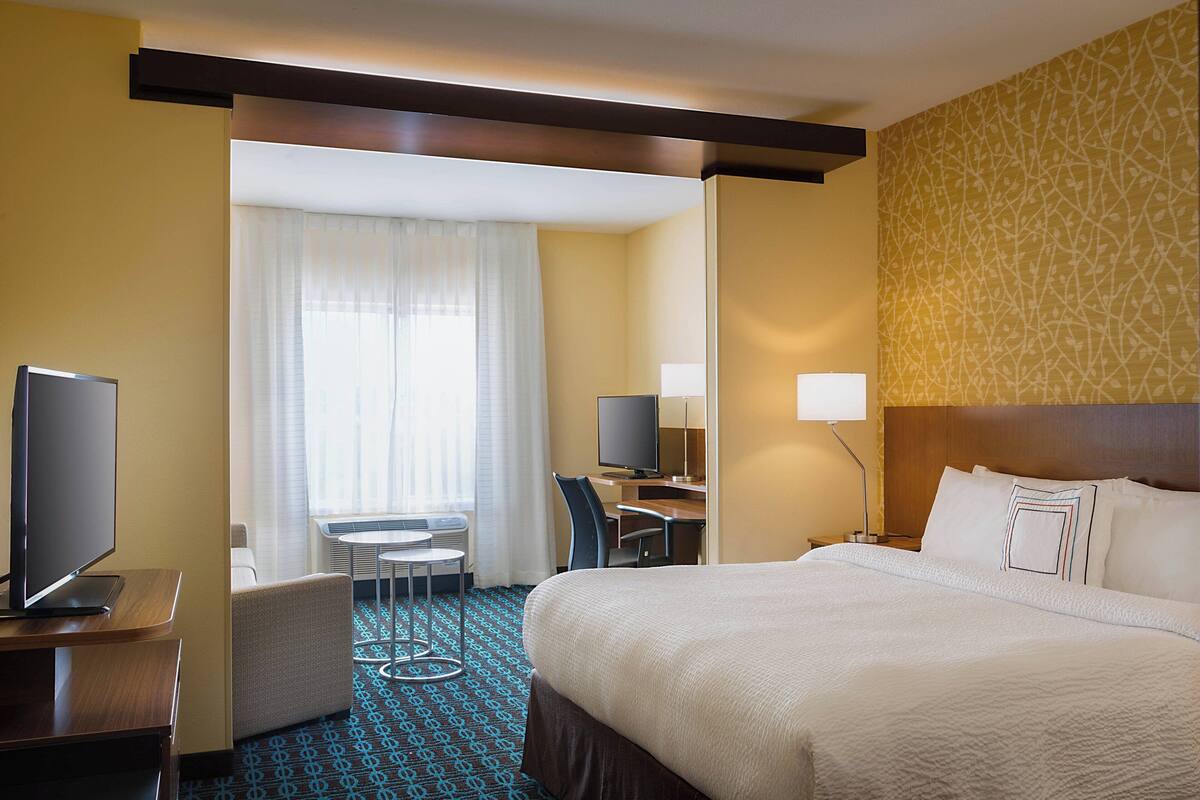 Ein Hotelzimmer mit einem großen Bett, einem Schreibtisch mit Stuhl, einem Fernseher und einem kleinen Tisch.