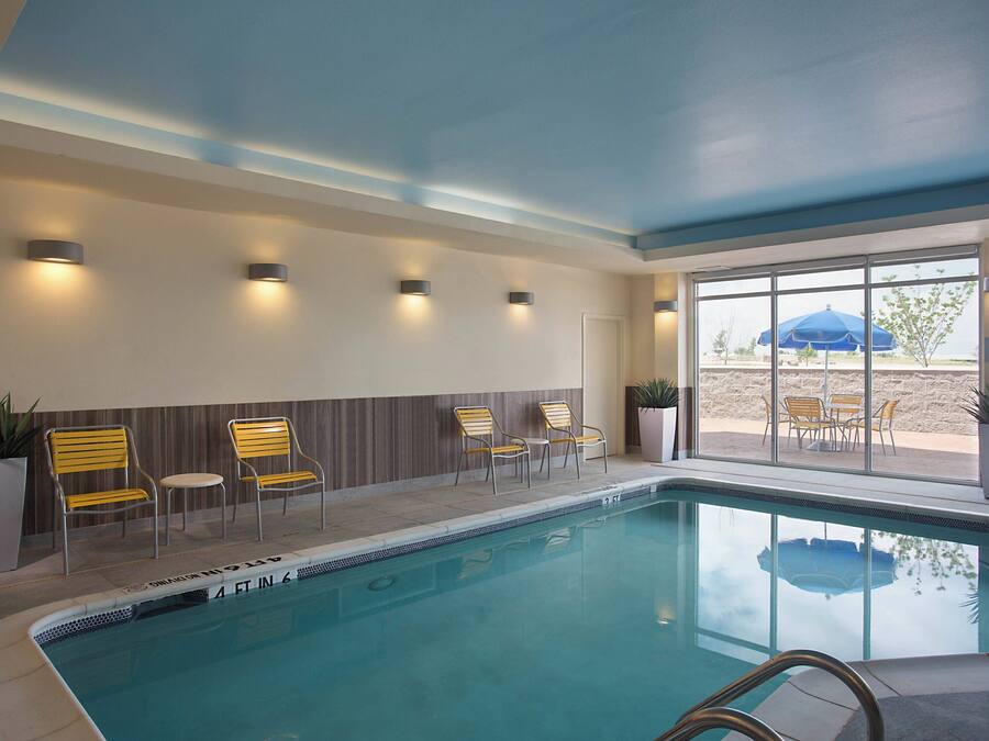 A swimming pool with chairs and potted plants, a ceiling with recessed lighting, and a view of the outdoors through large windows.