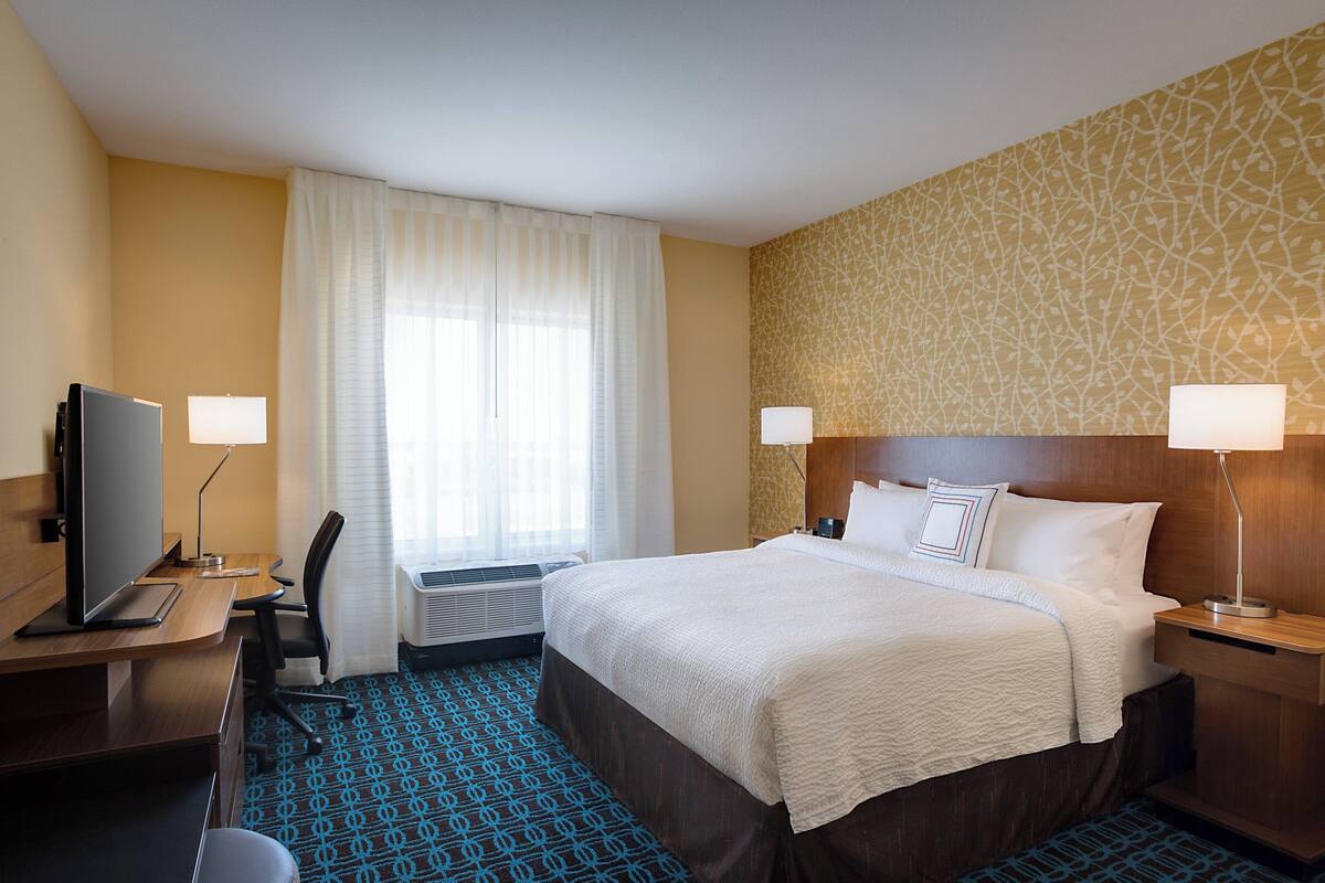 Ein Hotelzimmer mit Bett, Schreibtisch, Stuhl, Fernseher und Lampen.