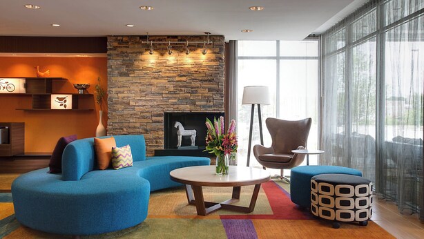 A modern living room with a stone fireplace, blue sofas, and a large window with sheer curtains. - Fairfield Inn & Suites Dallas West/i-30 (Dallas)