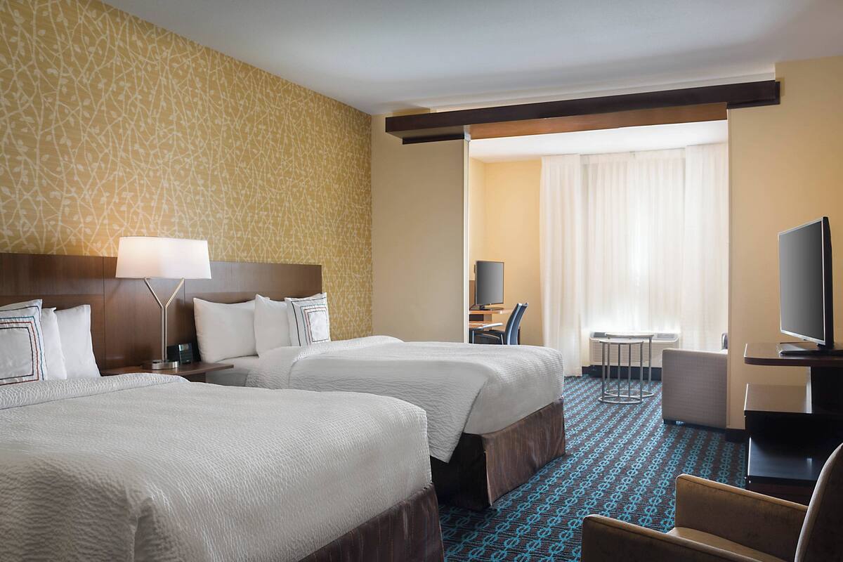 Ein Hotelzimmer mit zwei Betten, einem Schreibtisch, einem Stuhl, einem Fernseher und einem kleinen Tisch.