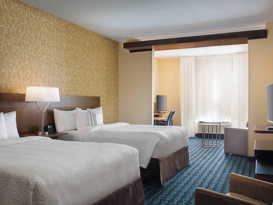 A hotel room with two beds, a desk, a chair, a television, and a small table.
