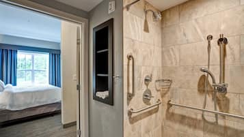 Habitació d'hotel amb zona de dutxa, un llit i una finestra amb cortines.