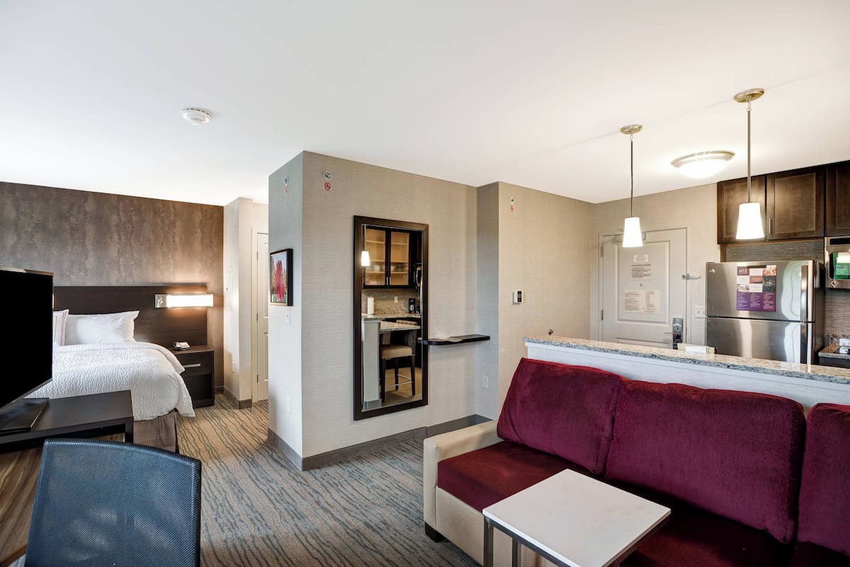 Une chambre d’hôtel comprenant un lit, un bureau, une chaise, un canapé, un coin cuisine et une salle de bain.