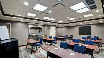 A conference room with multiple tables and chairs, a whiteboard, and a kitchenette area.