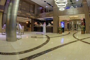 A modern hotel lobby with a reception desk, a large pillar, and a curved marble floor design. - National Park Hotel (Baljurashi)