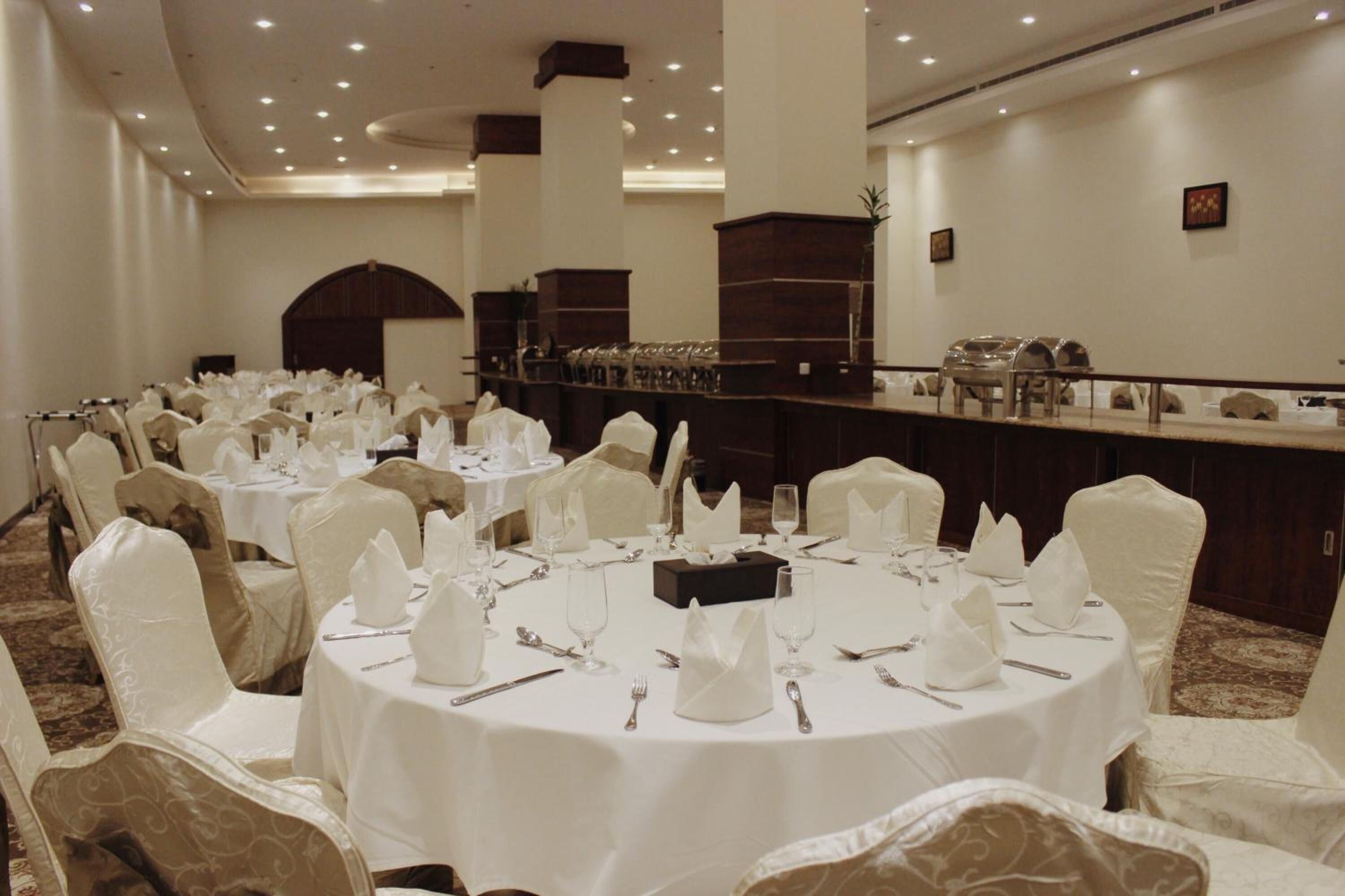 A banquet hall with round tables set for a formal event, featuring white tablecloths, folded napkins, and silverware.