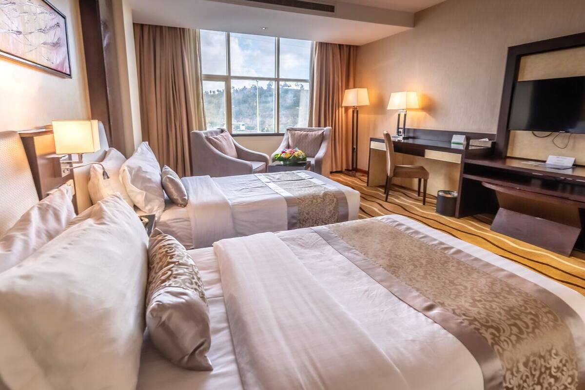 Ein Hotelzimmer mit zwei Betten, einem Schreibtisch, einem Stuhl und einem Fernseher.