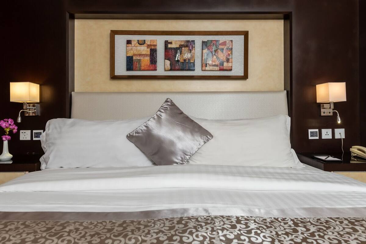 Ein Hotelzimmer mit einem großen Bett, zwei Nachttischlampen, einem gerahmten abstrakten Kunstwerk über dem Bett und einem Telefon auf dem Nachttisch.