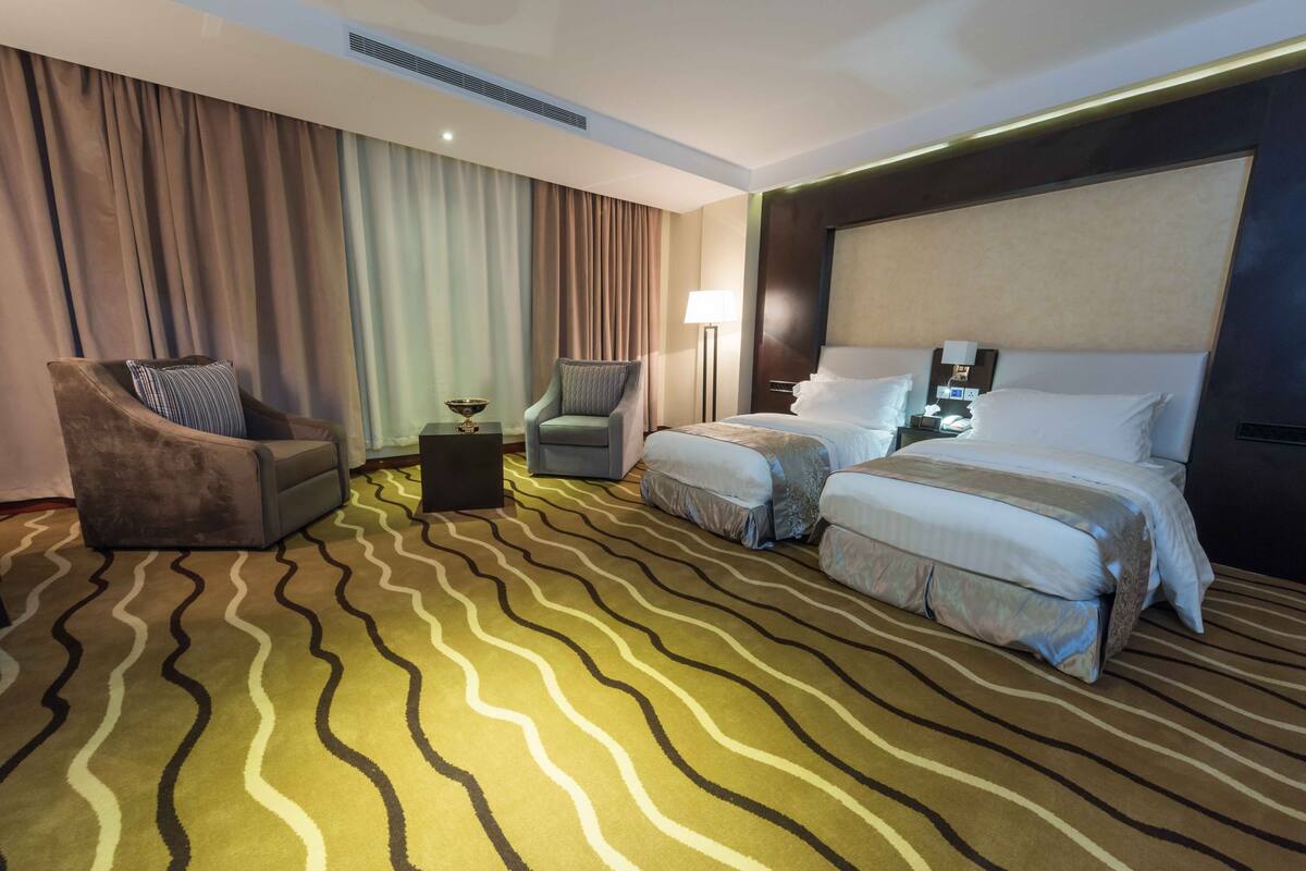 Ein Hotelzimmer mit einem großen Bett, zwei Nachttischen, einem Sessel und einem Teppich mit Muster.