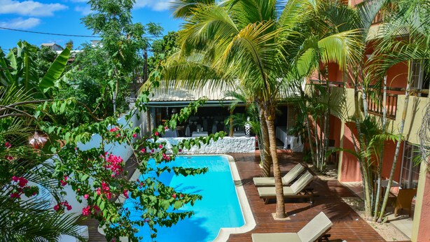 A swimming pool surrounded by palm trees and lounge chairs, with a building in the background. - La Margarita (Pointe Aux Piments)