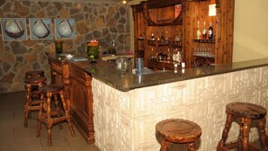 A bar area with a stone wall, wooden bar counter, stools, and various bottles and glasses. - La Margarita (Pointe Aux Piments)
