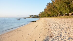 A sandy beach with footprints, calm water, and boats. Trees line the shore. - La Margarita (Pointe Aux Piments)