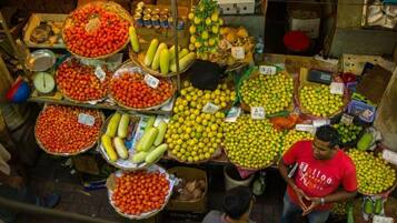 Un puesto de mercado con diversas frutas y verduras expuestas en cestas y cajas, con etiquetas de precios visibles.
