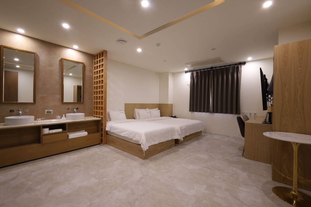 Une chambre d’hôtel moderne équipée d’un lit double, de deux tables de chevet, d’un grand miroir, d’une coiffeuse avec deux vasques et d’un bureau avec une chaise.