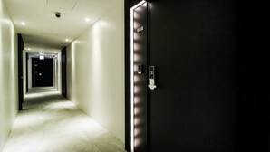 Un pasillo moderno de hotel con un ascensor elegante marcado '808' y un corredor bien iluminado que conduce a una habitación a oscuras.