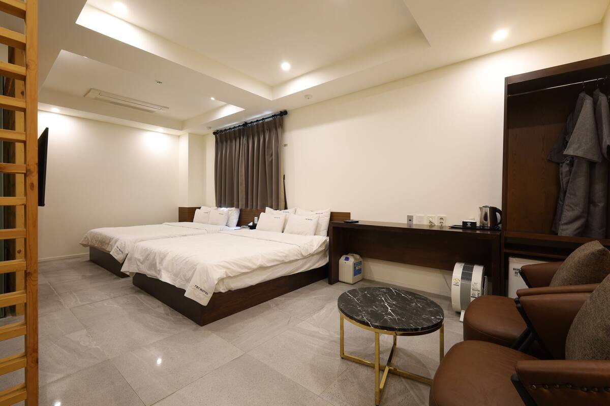 Une chambre d’hôtel avec un lit double, une petite table ronde, un coin salon avec un fauteuil, une armoire et un miroir.