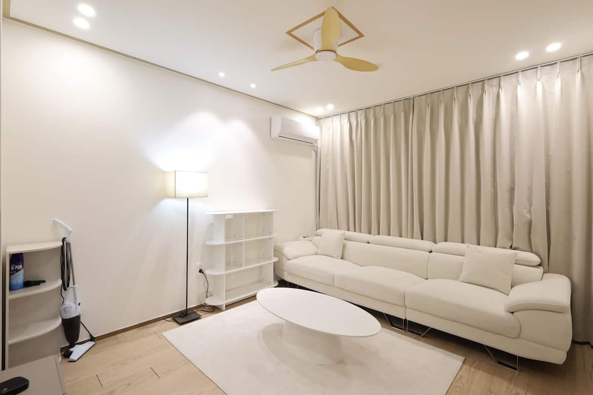 Un salon moderne avec un canapé blanc, une table basse, un lampadaire et un ventilateur de plafond.