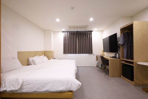 A hotel room with a double bed, a desk with a chair, a TV, and a wardrobe.