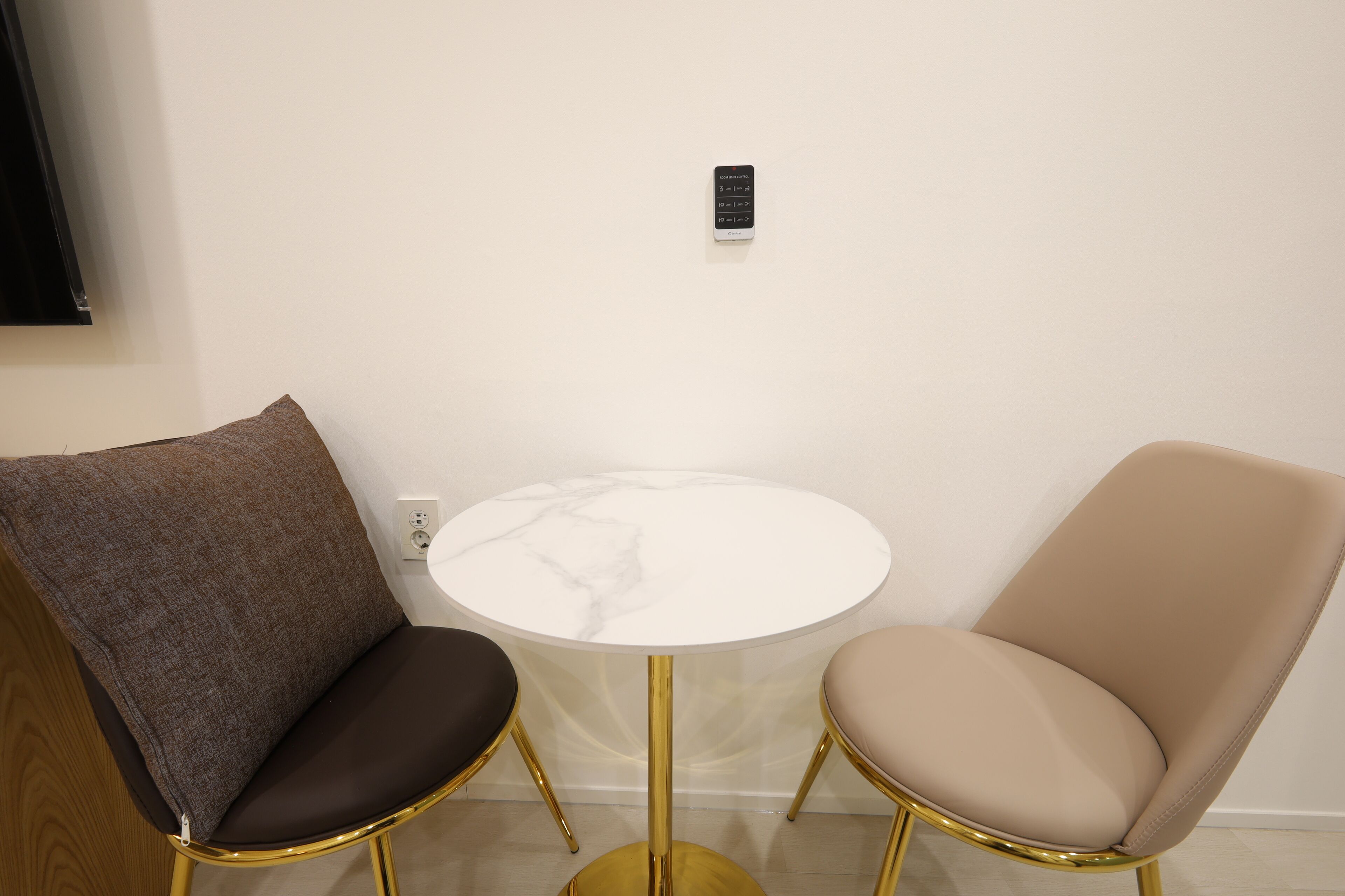 A small round table with a white marble top and gold legs, flanked by two chairs with brown and beige upholstery.