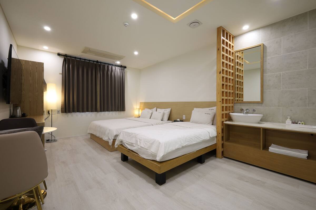 Une chambre d’hôtel avec deux lits, une coiffeuse en bois avec un lavabo, un miroir et un téléviseur fixé au mur.