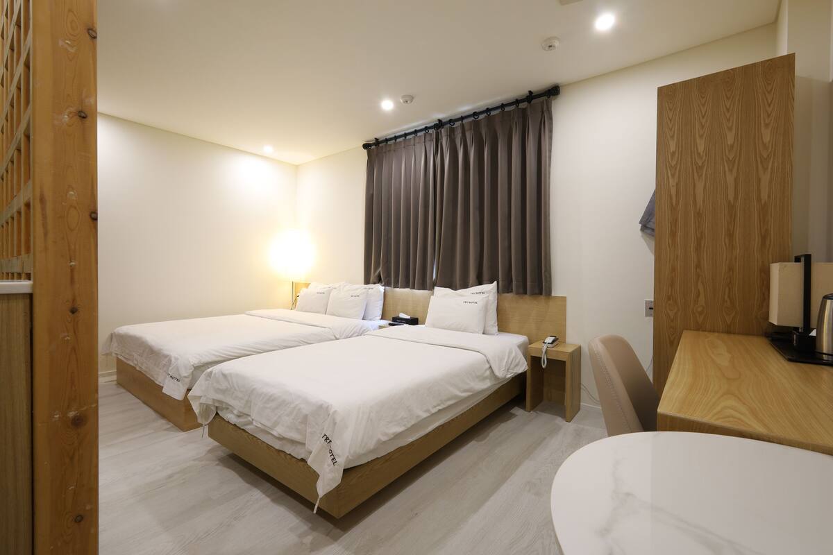 Une chambre d’hôtel avec deux lits, une tête de lit en bois, un bureau et une chaise.