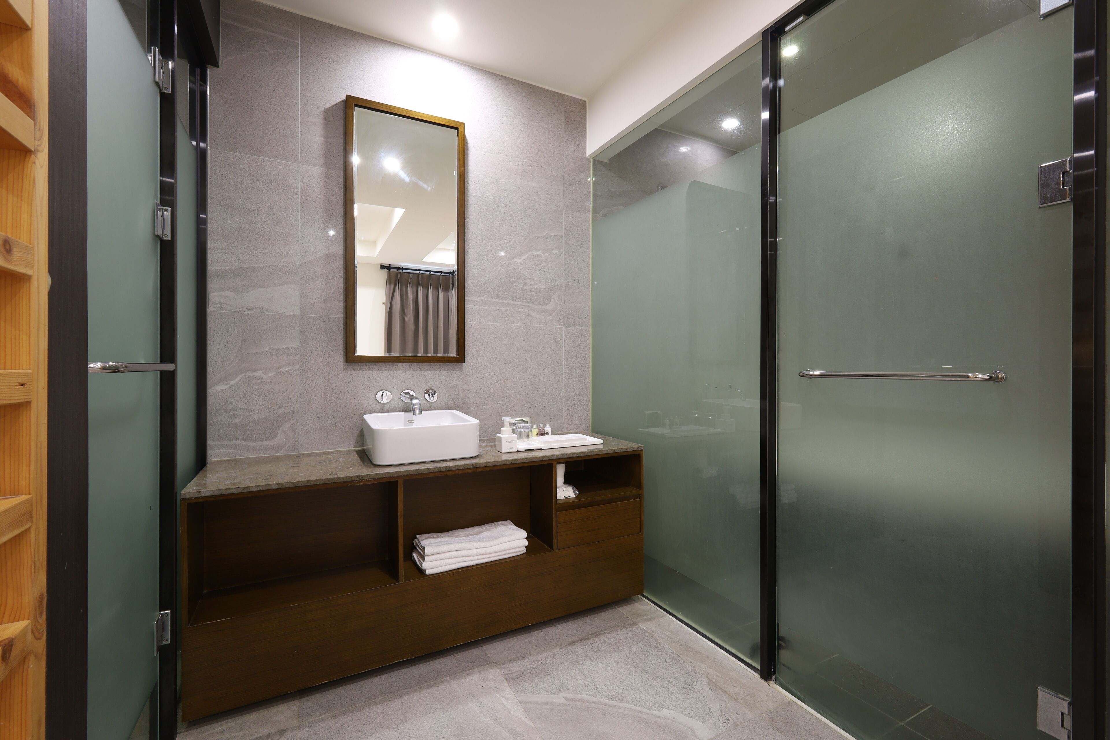 A modern bathroom with a glass shower enclosure, a wooden vanity with a sink, and a mirror above the vanity.