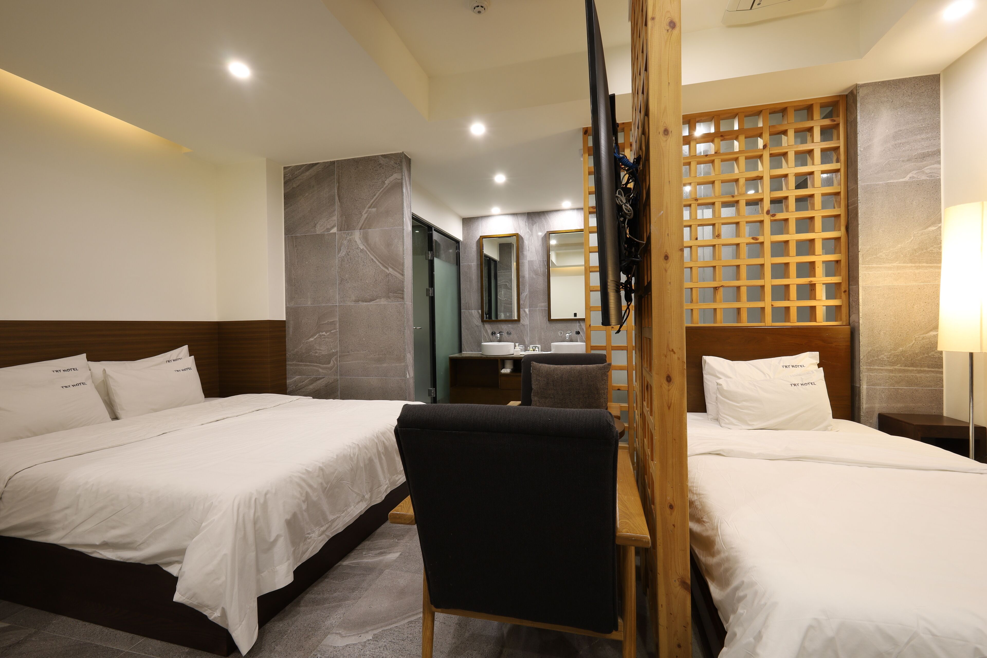 Habitación de hotel con dos camas, un escritorio, una silla, un espejo y un separador de madera.