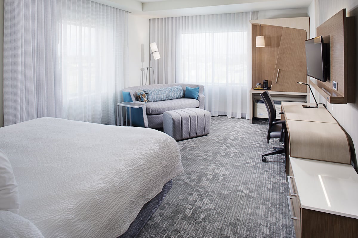 A hotel room with a large bed, a desk with a chair, a television, and a small table with a lamp.