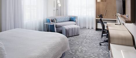 Ein Hotelzimmer mit einem großen Bett, einem Schreibtisch mit Stuhl, einem Fernseher und einem kleinen Tisch mit Lampe.