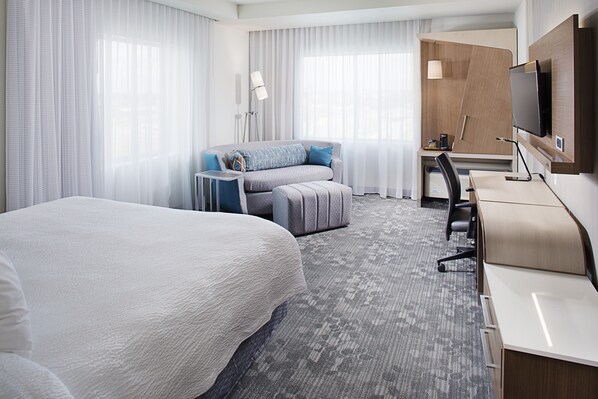 A hotel room with a large bed, a desk with a chair, a television, and a small table with a lamp.