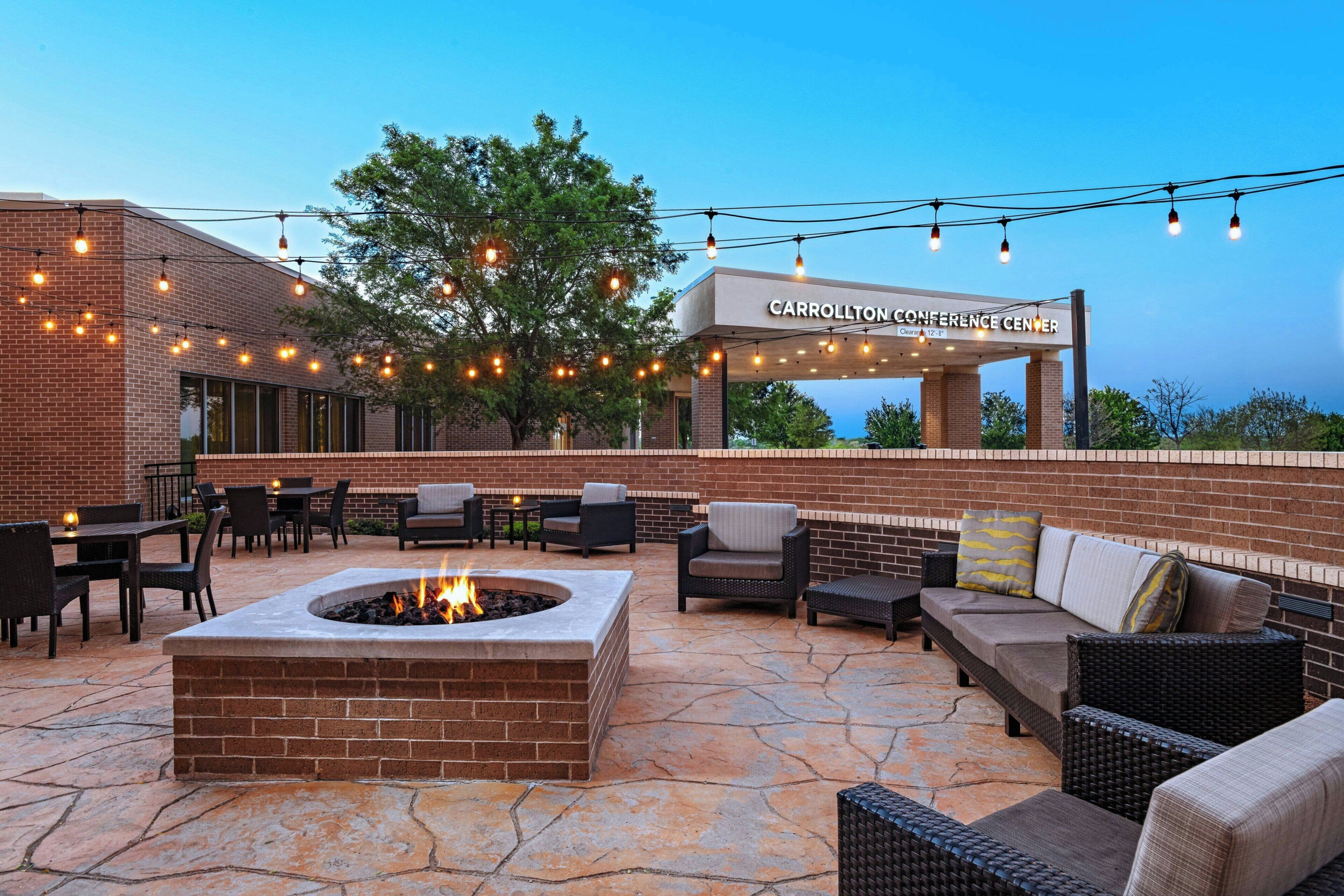 An outdoor patio area with a fire pit, seating, and string lights.