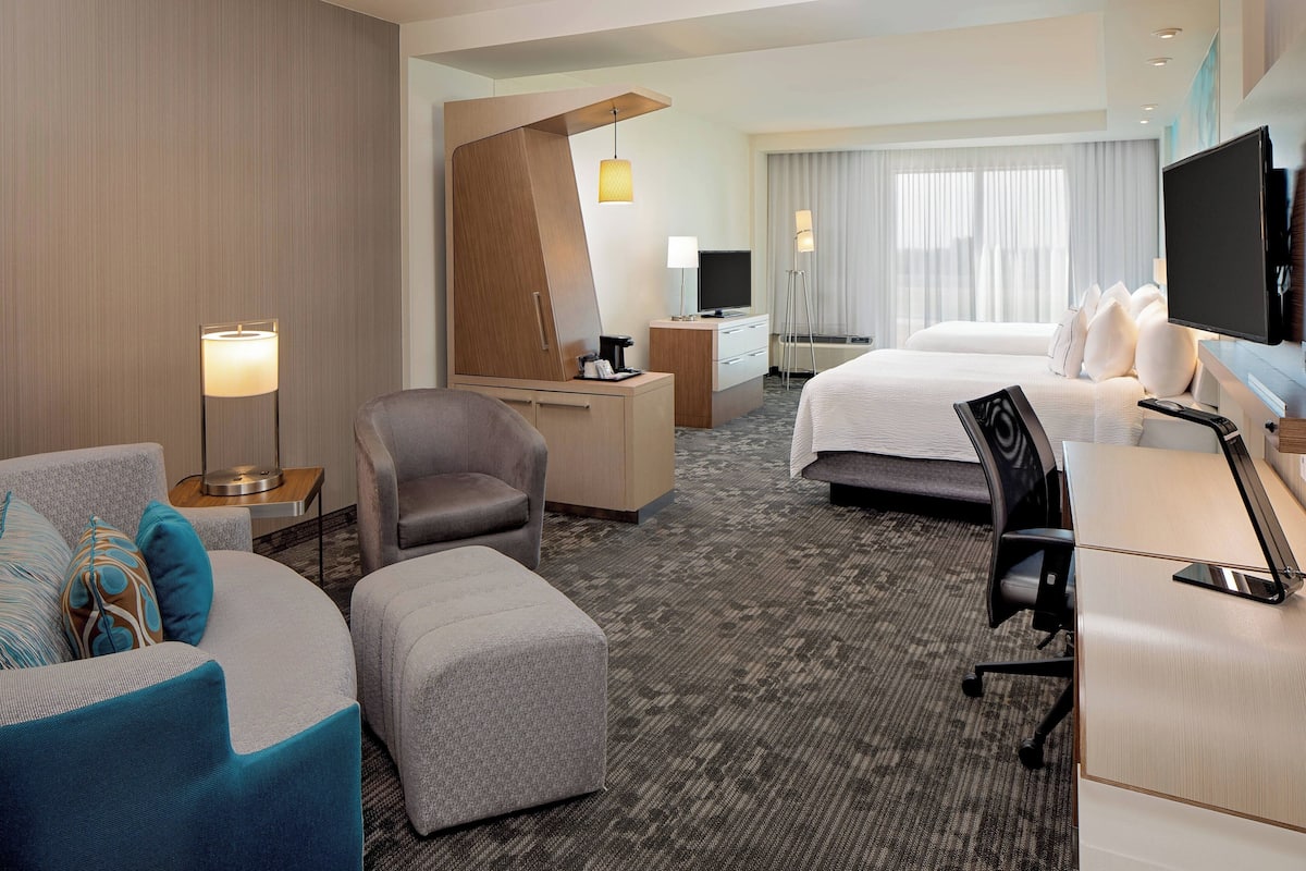 A hotel room with a bed, a desk with a computer, a chair, a sofa, and a TV.