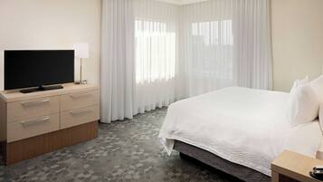 Una habitación de hotel con una cama, un televisor sobre una cómoda de madera y una ventana con cortinas de gasa.