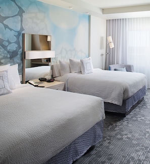 A hotel room with two beds, a desk with a lamp, a large mirror, and a view of the city.