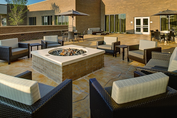 An outdoor patio area with wicker furniture, a fire pit, and umbrellas.