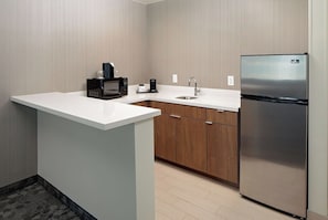 A compact kitchen with a microwave, coffee maker, sink, and stainless steel refrigerator.