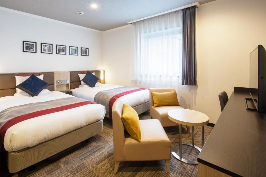 A hotel room with two beds, a small sofa, a round table, and a TV.