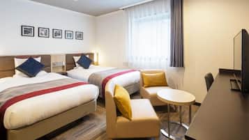 Habitación de hotel con dos camas, un pequeño sofá, una mesa redonda y un televisor.