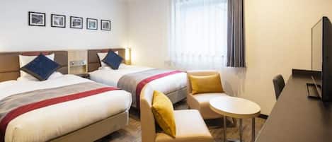 A hotel room with two beds, a small sofa, a round table, and a TV.