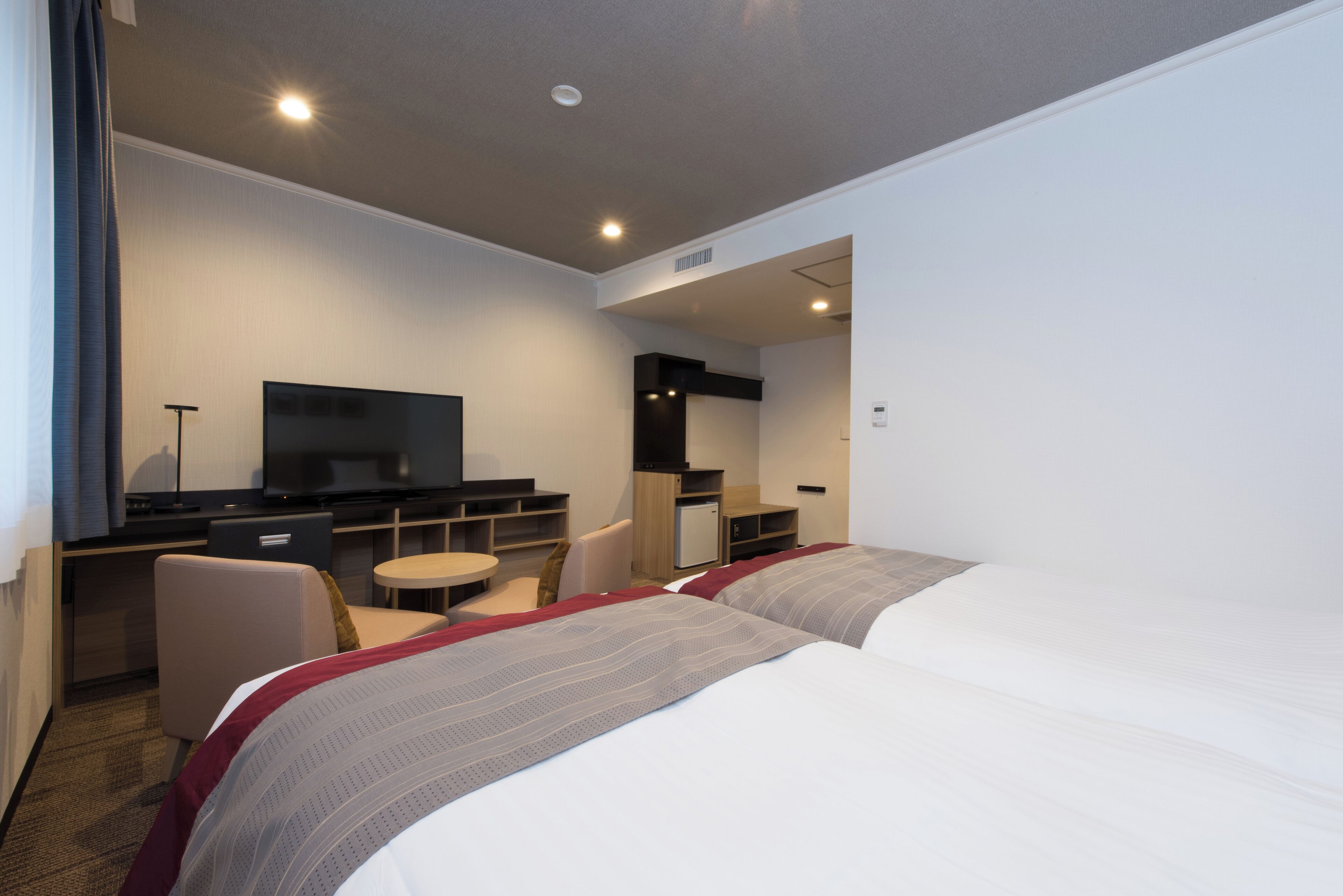 A hotel room with two beds, a desk with a television, a small table, and a chair.