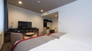 A hotel room with two beds, a desk with a television, a small table, and a chair.