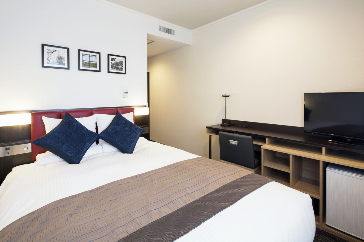 A hotel room with a bed, a TV, a desk, and a small cabinet.